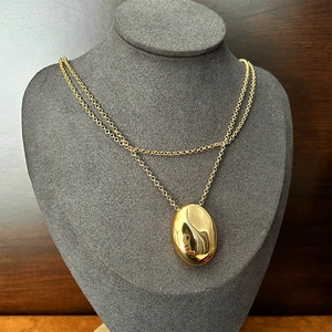 Detail view of a long gold double-layer necklace with a large oval water drop pendant