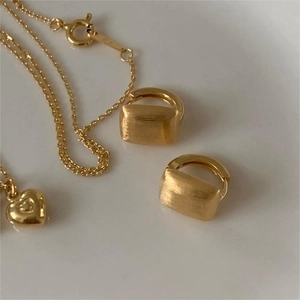 Close-up of matte brushed gold geometric hoop earrings and heart pendant necklace