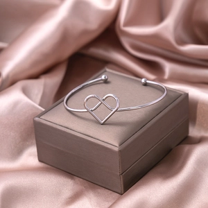 Detail of silver heart-shaped knot cuff bracelet on elegant champagne satin fabric