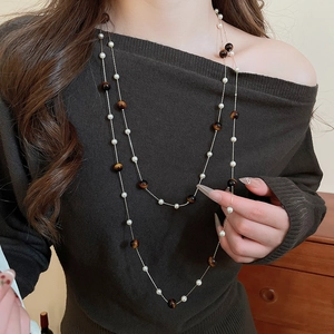 Détail d'un collier doré multicouche avec perles blanches et œil de tigre sur modèle