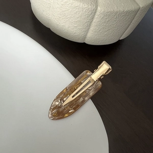Macro detail of amber acetate hair clip with gold glitter and metallic grip on ceramic