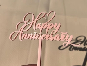 Close-up of pink acrylic Happy Anniversary cake topper on minimalist beige background
