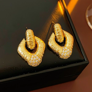 Detailed view of gold rhombus earrings with clear zircon stones on black leather