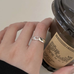 Detailed view of hollow heart silver ring worn while holding a coffee cup in soft light