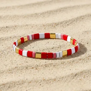 Detail of colorful bohemian tile beads bracelet on beach sand with sunlit shadows