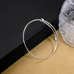 Detailed view of silver minimalist bangle with adjustable sliding buckle on black gold background