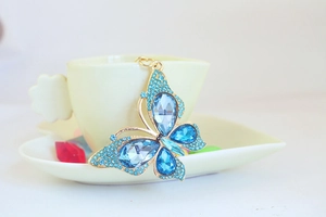 Close-up of a blue crystal butterfly keychain hanging on a beige ceramic coffee cup