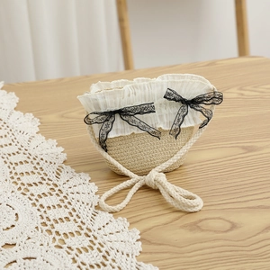 Détail du sac en paille avec bordure en dentelle blanche, nœuds noirs et anses en corde