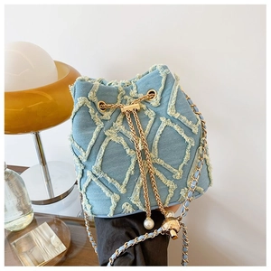 Detail of blue denim bucket bag with gold chain strap, drawstring, pearl and metal charms