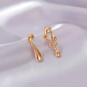 Macro detail of liquid gold asymmetrical teardrop earrings on purple silk fabric
