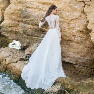 Elegant white chiffon wedding dress with lace embroidery back and long sleeves on a beach