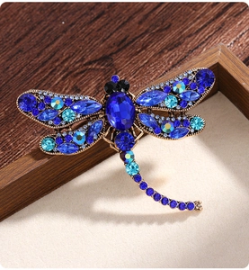 Detail of vintage dragonfly brooch with blue gems on a brown wooden frame