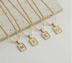 Detail of 18K gold plated square pendants with natural shell inlay and capital letters