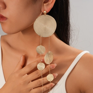 Detailed view of long gold textured tassel earrings worn by a model in studio setting