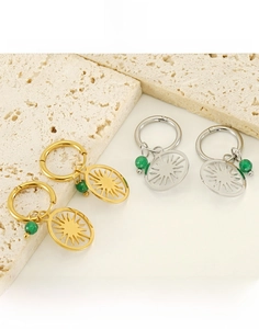 Detail of titanium steel sun earrings with green beads in gold and silver finish