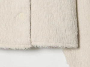 Detailed close-up of cream fuzzy plush fabric texture with elegant front buttons