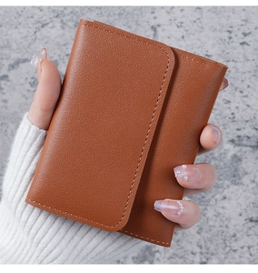 Brown leather tri-fold wallet held in hand, showing fine stitching and lychee texture