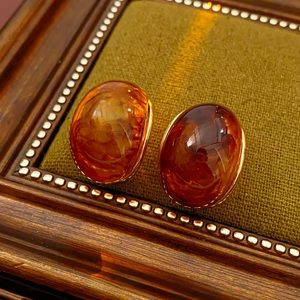 Close-up of amber resin earrings with gold edges on an elegant dark green velvet display