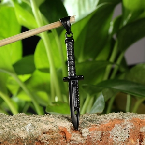 Men's black stainless steel dagger pendant necklace hanging over a rustic brick