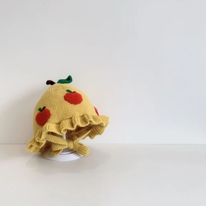Detailed close-up of yellow knit baby hat featuring apple pattern and ruffled edges
