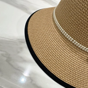 Détail du chapeau de paille avec garniture de perles blanches et bordure en ruban noir