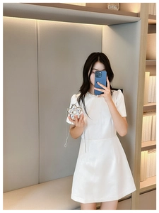 Detail of elegant white dress featuring pearl neckline and star-shaped silver chain bag