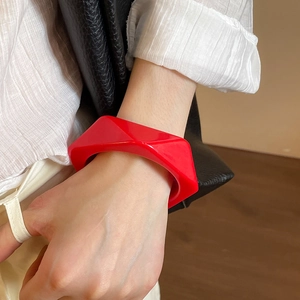 Close-up of a bright red irregular resin bangle worn on a wrist with a white shirt