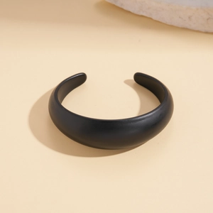 Macro detail of minimalist black matte acrylic open cuff bracelet on stone surface