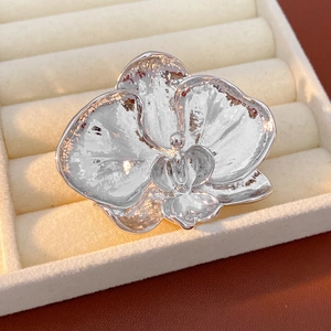 Detailed view of silver orchid brooch with textured metal petals in a beige velvet jewelry box