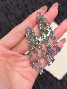 Close-up of dangling silver earrings with blue and green oval stones and tassels