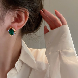 Dettaglio dell'orecchino vintage con strass smeraldo e montatura dorata sull'orecchio