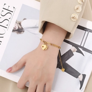 Detail of gold heart pendant bracelet with paperclip chain on a beige suit sleeve
