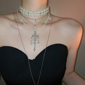 Detail of layered pearl and crystal cross necklace worn by model against black fabric