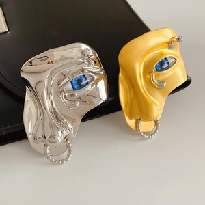 Detail view of surrealist face brooch with blue eye and metal nose ring on leather bag