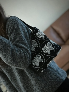 Detail of white butterfly embroidery on black canvas shoulder bag shown on model