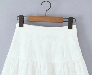 Détail d'une jupe blanche à taille haute avec broderies florales et texture plissée élégante