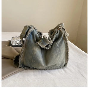 Detail of vintage washed denim tote bag featuring frayed edges and tassel design elements