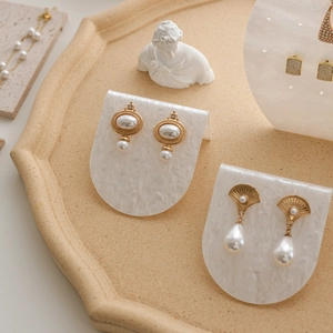Elegant gold pearl earrings displayed on a marble textured acrylic jewelry stand