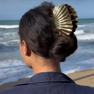 Detailed close-up of a golden shell-shaped hair claw clip worn in an outdoor beach setting