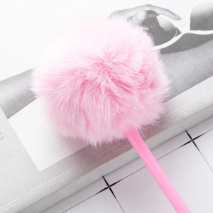 Cute pink plush ballpoint pen with soft faux fur pom pom decoration on grid background