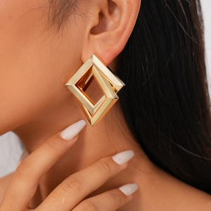 Close-up of woman wearing golden geometric square earrings with a metallic finish