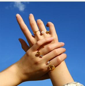 Close-up of gold heart rings with pearls and zircon worn against a clear blue sky