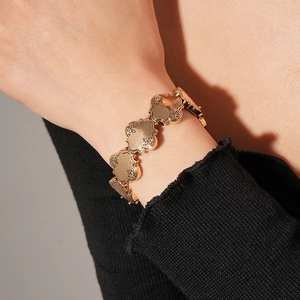 Détail d'un bracelet trèfle doré avec gravures vintage porté sur une manche noire