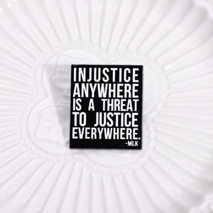 Macro shot of rectangular black enamel pin with MLK quote on a white ceramic tray