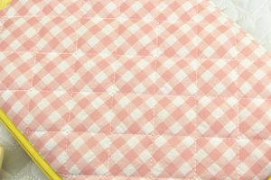 Close-up of pink checkered tablet sleeve with diamond quilting and yellow zipper detail