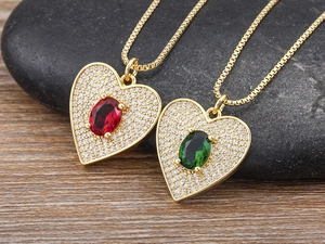 Macro shot of gold plated heart necklaces with red and green gems on wood texture