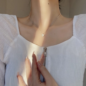 Close-up of minimalist silver heart necklace with shell inlay on female collarbone
