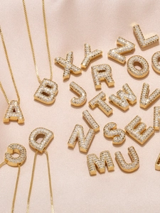 Makro-Detail von 18K vergoldeten Buchstabenanhängern mit weißen Zirkonia-Steinen