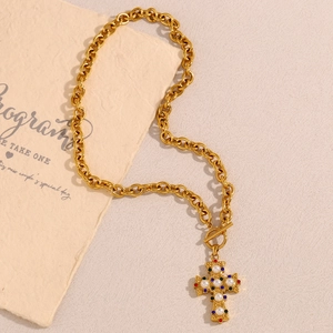 Close-up of golden cross necklace with colorful gemstones and pearls on toggle clasp