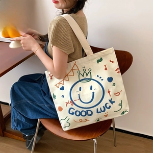 Cream canvas tote bag featuring a colorful smiley face graffiti and wide shoulder strap